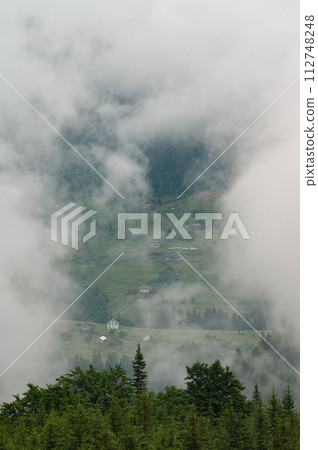 Dense fog in the mountains, through which the houses and the village are barely visible. 112748248