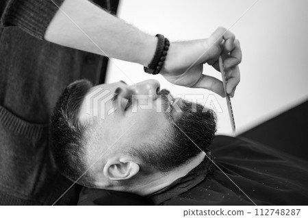 Barber combs beard with comb while shaving Caucasian man Barber combs beard with comb while shaving Caucasian man 112748287