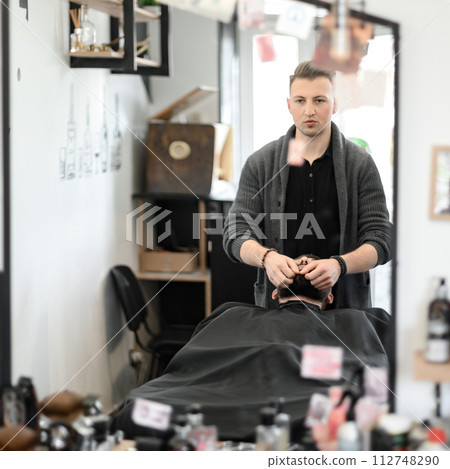 A barber massages and rubs a male client beard after applying moisturizing oil A barber massages and rubs a male client beard after applying moisturizing oil 112748290