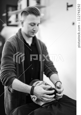 A barber massages and rubs a male client beard after applying moisturizing oil 112748292