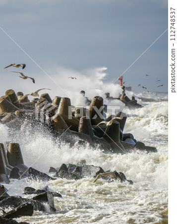 Storm at sea, high waves crashing against the concrete breakwaters of the port, white splashes 112748537