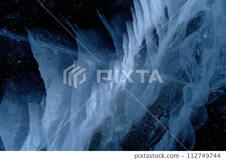Transparent dark blue ice of frozen Baikal lake with white cracks pattern. Beautiful winter nature background. Great backdrop for your design with copy space. 112749744
