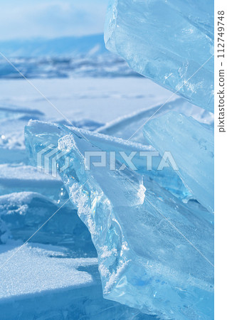 Ice hummocks against blue sky and mountains on Baikal Lake. Transparent blue ice floe. Natural background. Great backdrop for your design with copy space. 112749748