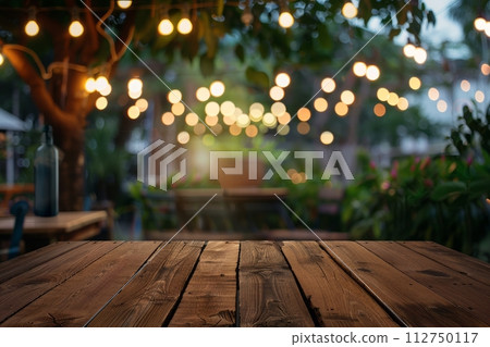 Front wooden plank table against a bright blurred cafe background with glowing street lanterns in the evening 112750117