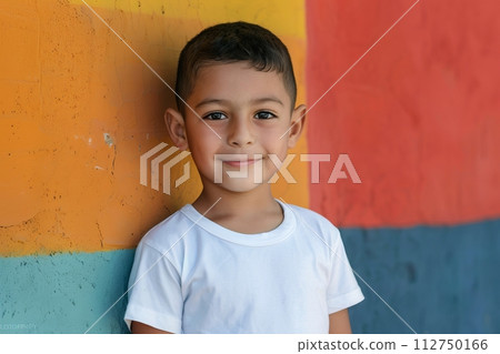 Hispanic child boy 4-6 years old in a white T-shirt without a pattern against the background of a colored wall 112750166