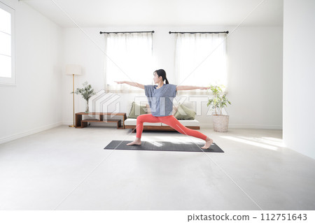 一個女人在美麗的背光客廳練習瑜珈的全身，戰士姿勢，廣角 112751643