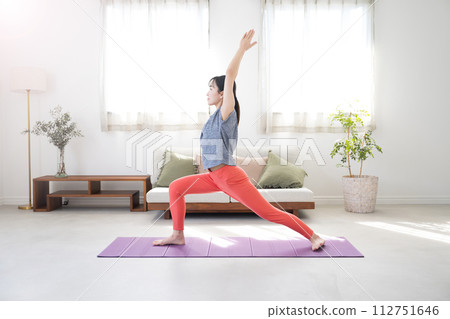 A woman doing yoga in a beautiful backlit living room, warrior pose 112751646