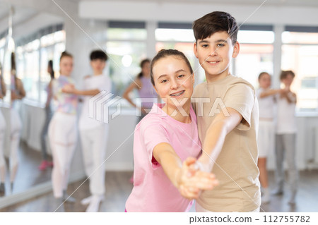 Group of positive teenagers learning to dance tango in dance studio Group of positive teenagers learning to dance tango in dance studio 112755782