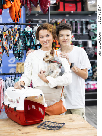 Mom and son choose pet carrier for small animal nursling dog of dwarf breed Yorkshire Terrier Mom and son choose pet carrier for small animal nursling dog of dwarf breed Yorkshire Terrier 112755854