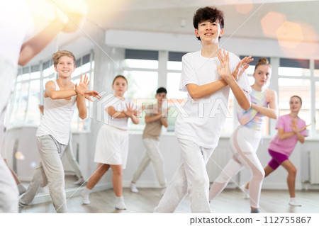 Male boy student repeats movements of unrecognizable teacher during group modern dance class. Male boy student repeats movements of unrecognizable teacher during group modern dance class. 112755867