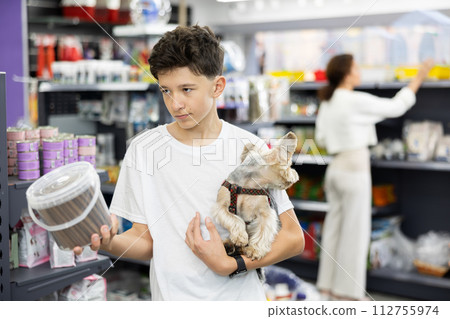Boy with dog Yorkshire terrier in arms and read composition of product at packaging of dog dry food 112755974