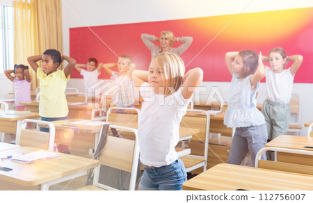 Preteen pupils doing warm-up in class with teacher at lesson 112756007