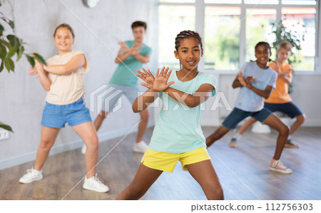 Positive juvenile girl engaged in Breakdancing in training room with children's group Positive juvenile girl engaged in Breakdancing in training room with children's group 112756303