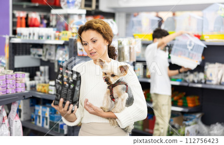 Woman with Yorkshire terrier choosing dry dog food in pet store Woman with Yorkshire terrier choosing dry dog food in pet store 112756423