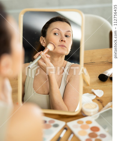 Woman applying facial makeup using blush brush Woman applying facial makeup using blush brush 112756435