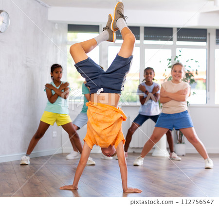 Positive juvenile boy engaged in Breakdancing in training room with children's group Positive juvenile boy engaged in Breakdancing in training room with children's group 112756547