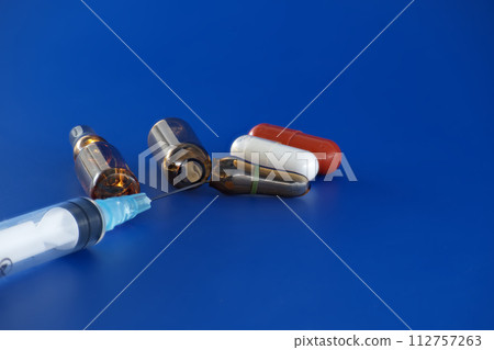 Syringe alongside a few vials of medicine and pills 112757263