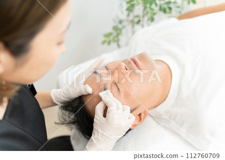Man wiping off permanent makeup, adjusting eyebrows at eyebrow salon, men's eyebrow salon, beauty eyebrow salon 112760709