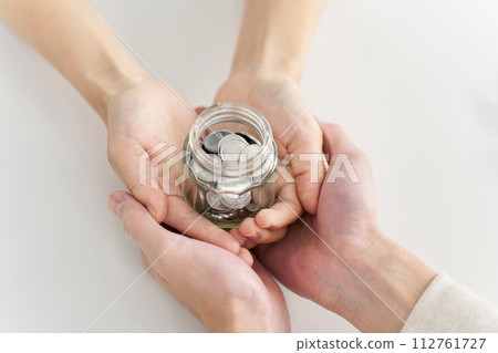 Hands of a man and woman carrying a jar containing coins 112761727