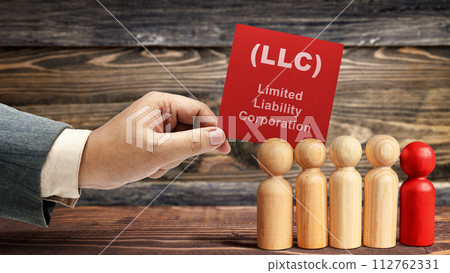 Business hand holding a note with LLC text, the acronym of Limited Liability Company with a row of wooden peg dolls 112762331