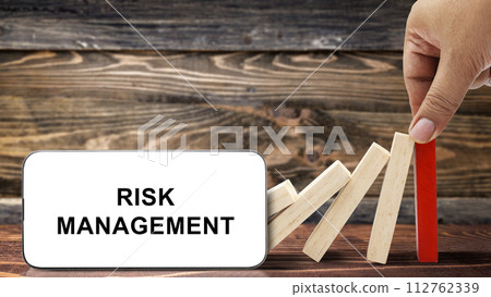 Business hand stopping a falling wooden dominoes with risk management text on the mobile phone screen Business hand stopping a falling wooden dominoes with risk management text on the mobile phone screen 112762339