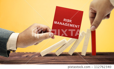 Business hand stopping a falling wooden dominoe with risk management text on the note Business hand stopping a falling wooden dominoe with risk management text on the note 112762340
