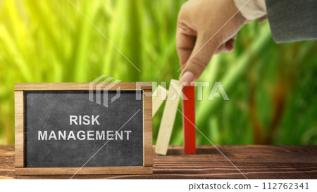Business hand stopping a falling wooden dominoe with risk management text on the chalkboard Business hand stopping a falling wooden dominoe with risk management text on the chalkboard 112762341