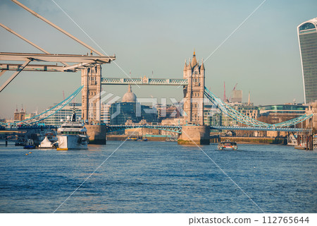 Sunny day at London's Tower Bridge with the River Thames in view, featuring boats and the distant dome of St Paul's Cathedral, highlighting the city's historic architecture. Sunny day at London's Tower Bridge with the River Thames in view, featuring boats and the distant dome of St Paul's Cathedral, highlighting the city's historic architecture. 112765644