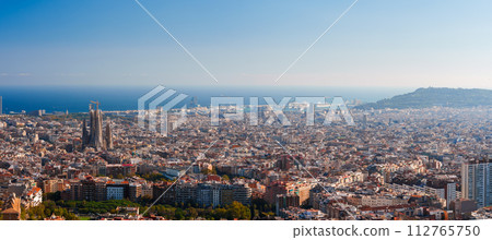 Panoramic view of Barcelona's skyline featuring the Sagrada Familia under a clear sky, with the Mediterranean Sea and port visible, showcasing the city's mix of architecture and natural landscape. 112765750