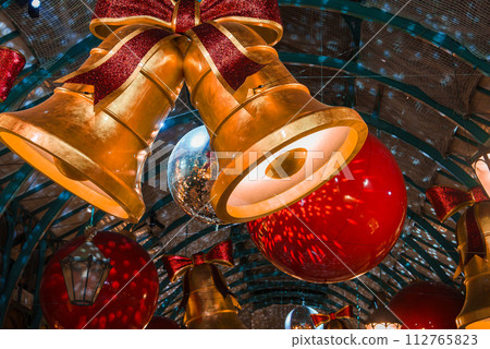 Giant golden bells and red baubles adorn an arched interior in London, creating a warm, festive ambiance that captures the joy of Christmas with traditional, opulent decorations. Giant golden bells and red baubles adorn an arched interior in London, creating a warm, festive ambiance that captures the joy of Christmas with traditional, opulent decorations. 112765823