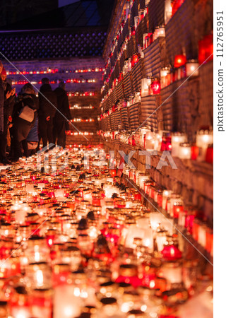 A solemn gathering in Latvia with small candles in red holders, symbolizing unity and remembrance, as people in warm clothes observe a moment of silence for Independence Day. 112765951