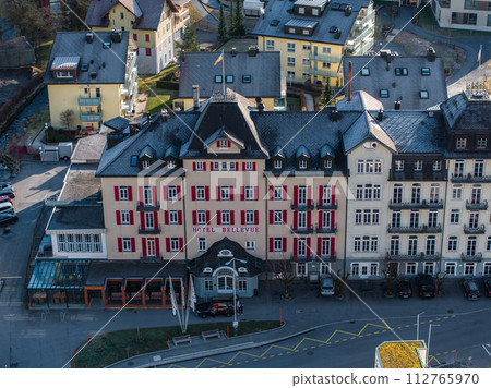 Aerial view of the grand Hotel Bellevue with a red facade in Engelberg, featuring a European alpine design, whitetrimmed windows, and a semicircular canopy entrance. 112765970