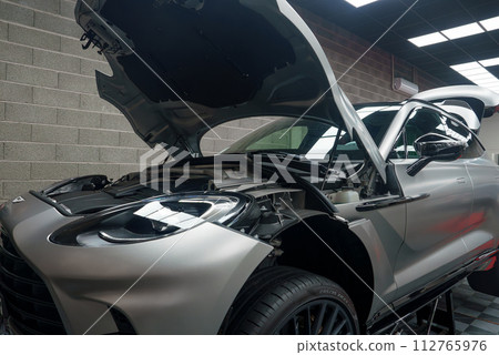 Luxury sports car in a professional garage with an open hood for maintenance, showcasing a clean engine bay and highperformance tires, suggesting meticulous care. 112765976