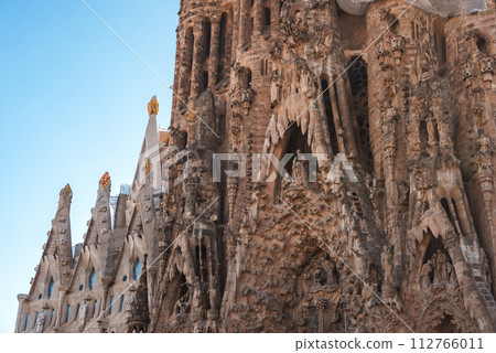 Closeup view of Sagrada Familia's detailed facade with sculptures and gothic elements in Barcelona, Spain, under a clear blue sky, showcasing Gaudi's iconic design. 112766011