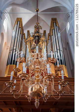 Elegant multitiered chandelier with intricate metalwork hangs in a European church, complemented by a symmetrical pipe organ in the background, likely in Copenhagen or Malmo. 112766226