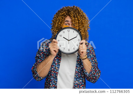 Serious strict stylish man holding office clock hiding behind checking time on watch obscuring face 112766305