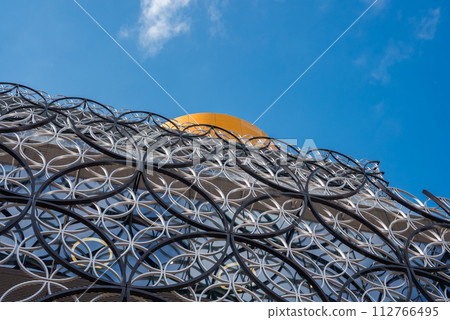 Closeup of the Library of Birmingham's metallic facade with interlocking circles and a bright yellow sphere against a clear blue sky, showcasing its modern design. Closeup of the Library of Birmingham's metallic facade with interlocking circles and a bright yellow sphere against a clear blue sky, showcasing its modern design. 112766495