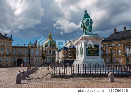 A historic European square features an oxidized bronze equestrian statue on a stone pedestal, surrounded by classical buildings with a baroque dome, likely in Copenhagen. A historic European square features an oxidized bronze equestrian statue on a stone pedestal, surrounded by classical buildings with a baroque dome, likely in Copenhagen. 112766536