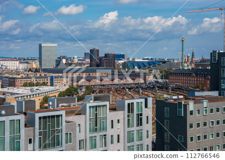 Overlooking a cityscape, modern homes with sleek designs beside a classic redroofed structure, likely in Copenhagen. Partly cloudy skies and active construction suggest expansion. Overlooking a cityscape, modern homes with sleek designs beside a classic redroofed structure, likely in Copenhagen. Partly cloudy skies and active construction suggest expansion. 112766546