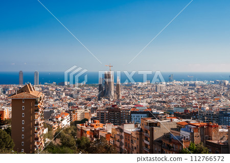 Panoramic view of Barcelona's cityscape featuring the unfinished Sagrada Familia under a clear blue sky, with a backdrop of the Mediterranean Sea and a mix of architectural styles. Panoramic view of Barcelona's cityscape featuring the unfinished Sagrada Familia under a clear blue sky, with a backdrop of the Mediterranean Sea and a mix of architectural styles. 112766572
