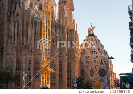 Barcelona's Sagrada Familia, designed by Antoni Gaudi, basks in dawn or dusk light, with intricate facades and a construction crane, hinting at its perpetual incompletion. 112766596