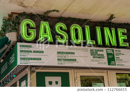 Bright, vivid green neon GASOLINE sign perched above a menu that lists burgers, featuring vegetarian choices, all within a retro diner ambiance, possibly located in Copenhagen or Malmo. 112766655