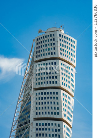 A modern, twisting skyscraper soars into the clear blue sky with wispy clouds in Malmo, Sweden. The Turning Torso's white facade and grid of windows highlight its dynamic, spiraling architecture. A modern, twisting skyscraper soars into the clear blue sky with wispy clouds in Malmo, Sweden. The Turning Torso's white facade and grid of windows highlight its dynamic, spiraling architecture. 112766836