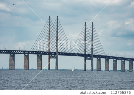 Capturing the sleek Oresund Bridge connecting Copenhagen, Denmark, to Malmo, Sweden, this image highlights the modern design with tall pylons and a web of cables against an overcast sky. 112766876