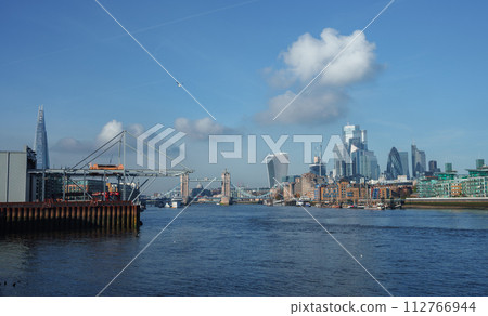 Panoramic view of the River Thames with the London skyline, featuring the Shard, Tower Bridge, and modern skyscrapers under a clear blue sky. No signs of activity or holiday decor. 112766944