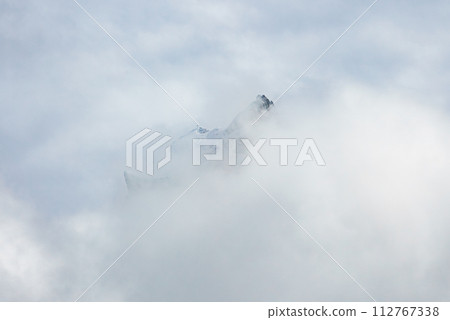 Misty mountain peaks emerge through clouds at Engelberg, with glimpses of a ski lift system, highlighting the serene Swiss Alps winter landscape and skiing ambiance. 112767338