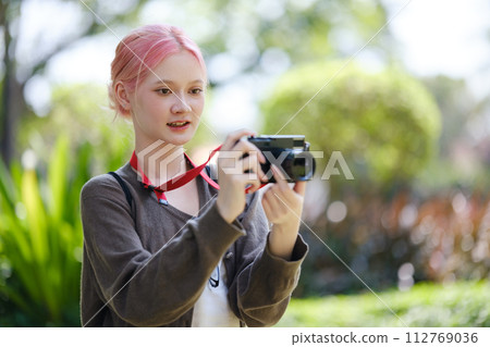 Beautiful Young artist Woman taking photo in flowers garden. Young cute girl carry the camera in the garden. Beautiful Young artist Woman taking photo in flowers garden. Young cute girl carry the camera in the garden. 112769036