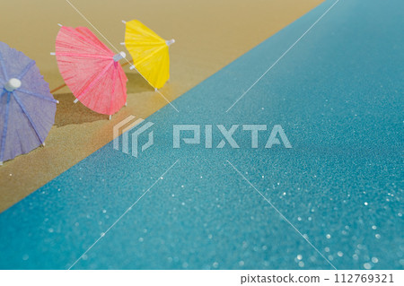 Abstract beach with glitter paper sand and water and cocktail umbrellas Abstract beach with glitter paper sand and water and cocktail umbrellas 112769321