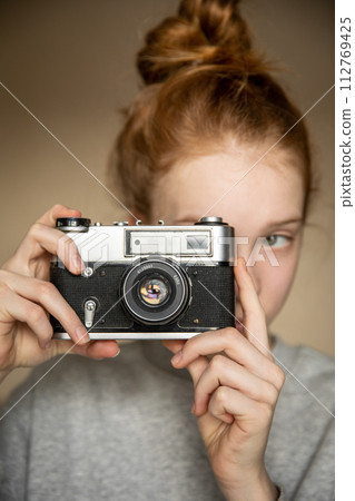 Film retro camera in the beautiful hands of a young red-haired girl 112769425