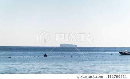 Calm blue sea with the silhouette of a large ship on the horizon 112769521